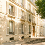 Appartement bordelais lumineux aux volets extérieurs, bordé d’arbres de rue sous une forte chaleur estivale.