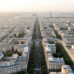 Vue aérienne réaliste de Paris au matin, montrant les immeubles haussmanniens, les toits urbains, les boulevards arborés et les quartiers de l’est baignés d’une lumière douce.