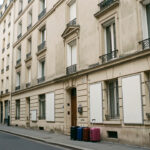 Rue urbaine française bordée d'immeubles résidentiels, avec quelques valises et des panneaux de location vierges près des entrées.