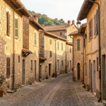Ancien village italien perché sur une colline, avec des maisons en pierre à rénover, des ruelles étroites et une lumière méditerranéenne chaleureuse.
